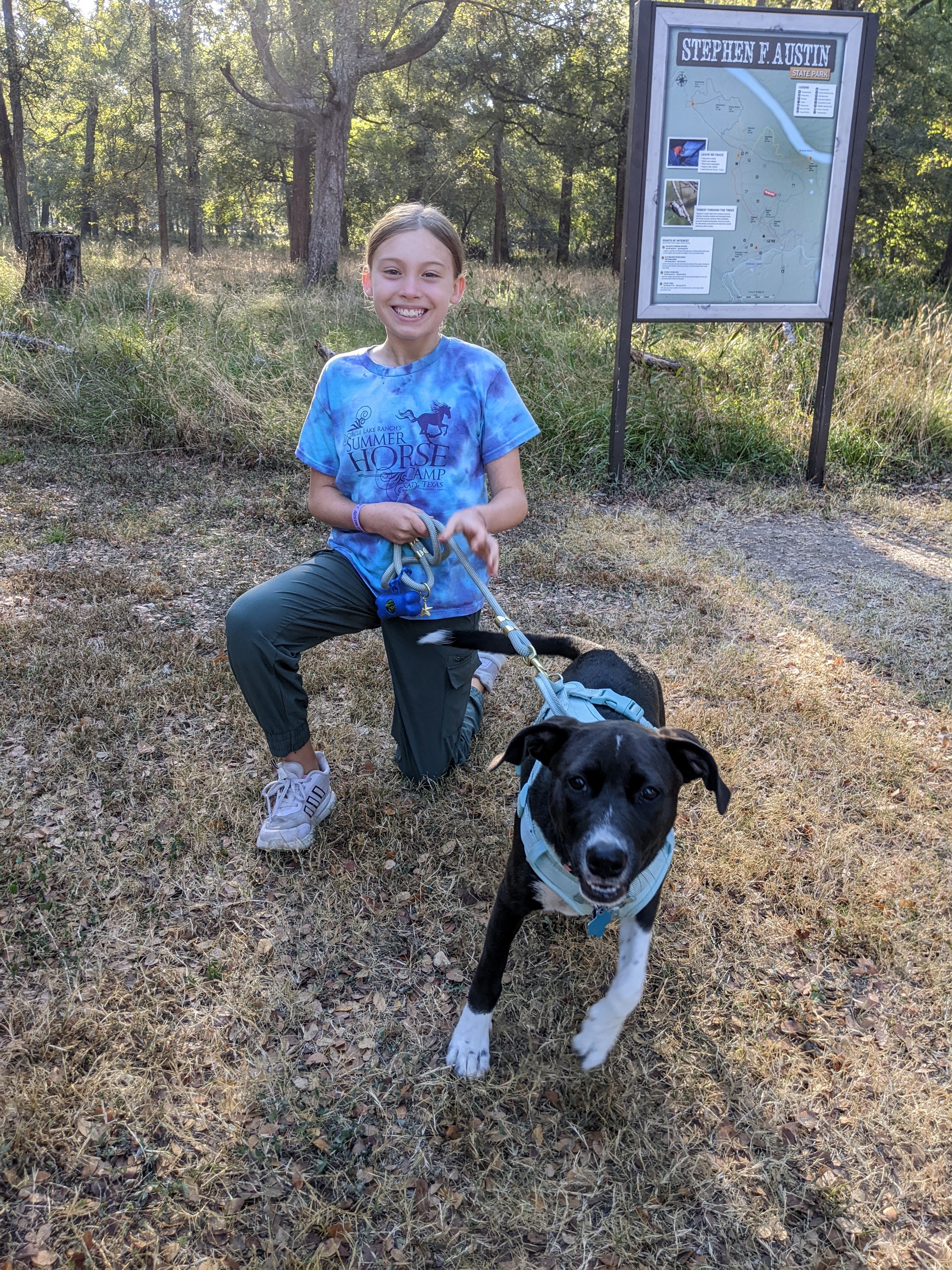 Young child and puppy smiling at the camera with Stephen F. Austin State Park trails sign in the background during a family camping trip.